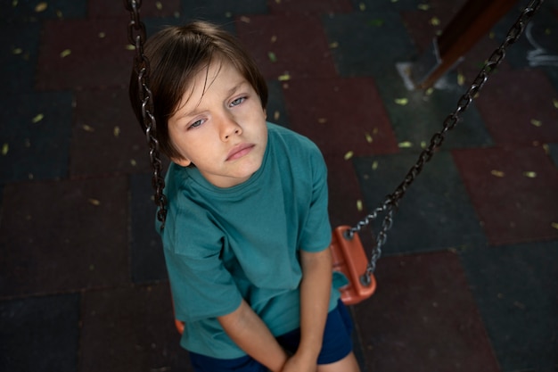 Foto gratuita niño triste de alto ángulo sentado en el columpio