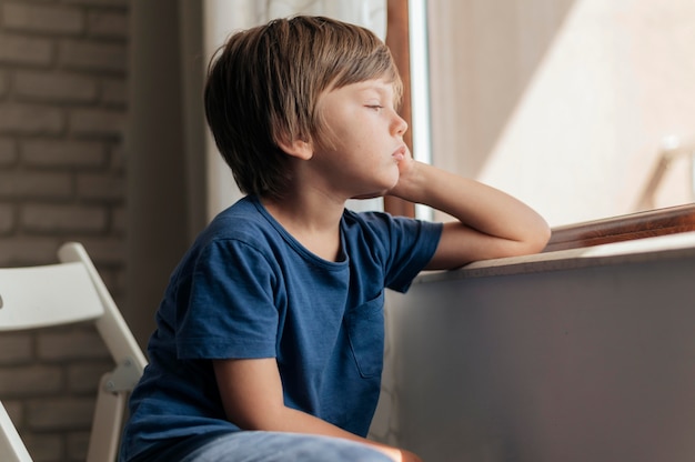 Niño triste mirando por la ventana durante la cuarentena