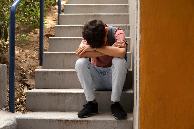 Niño triste sentado en las escaleras tiro completo