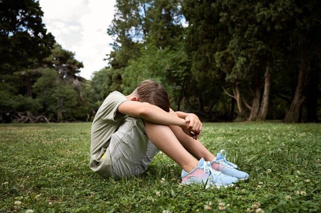 Niño triste sentado en la hierba tiro completo