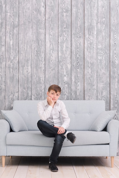 Niño triste sentado en el sofá en casa mirando la cámara