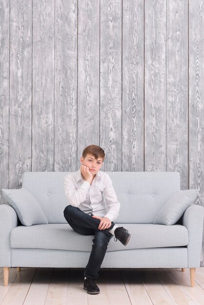 Niño triste sentado en el sofá en casa mirando la cámara