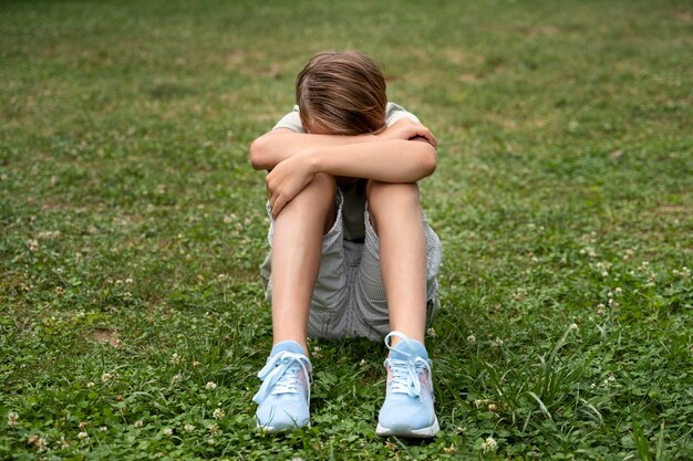 Niño triste de tiro completo sentado en la hierba