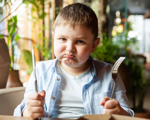 Niño triste de tiro medio con cubiertos