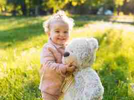 Foto gratuita niño vestido con ropa rosa y oso de peluche en el parque