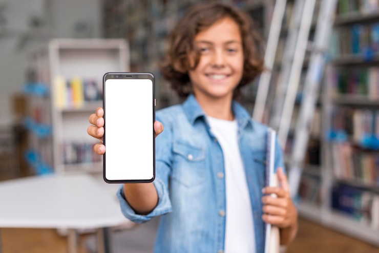 Foto gratuito niño de vista frontal sosteniendo un teléfono de pantalla vacía en la biblioteca