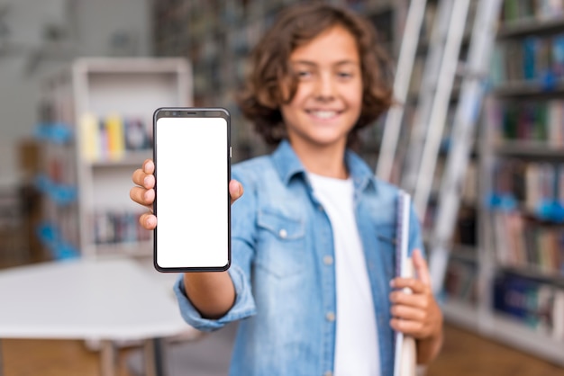 Niño de vista frontal sosteniendo un teléfono de pantalla vacía en la biblioteca