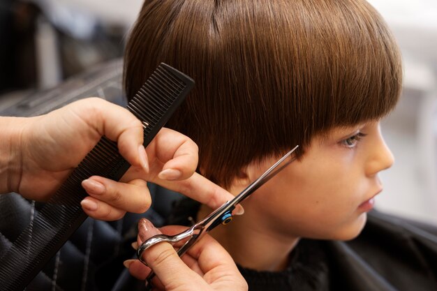 Niño de vista lateral cortándose el pelo en el salón