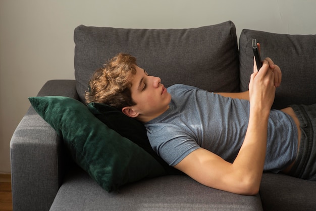 Niño de vista lateral revisando su teléfono mientras se queda en el sofá