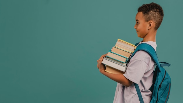 Niño de vista lateral sosteniendo una pila de libros copia espacio