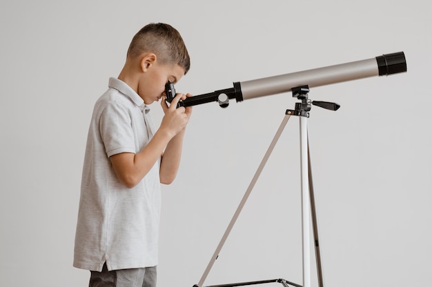 Niño de vista lateral usando un telescopio en clase