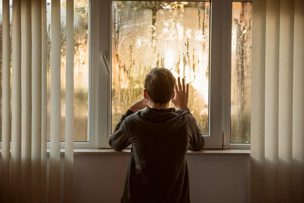 Niño de vista posterior de pie junto a las ventanas