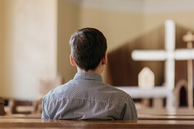 Niño de vista posterior rezando en la iglesia