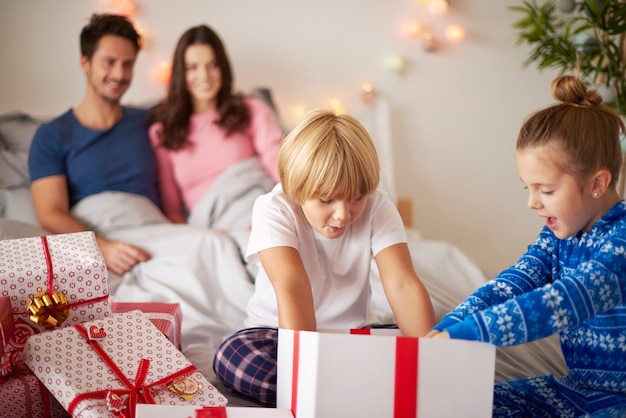 Niños abriendo regalos de Navidad en la cama.