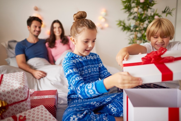 Niños abriendo regalos de Navidad en la cama.