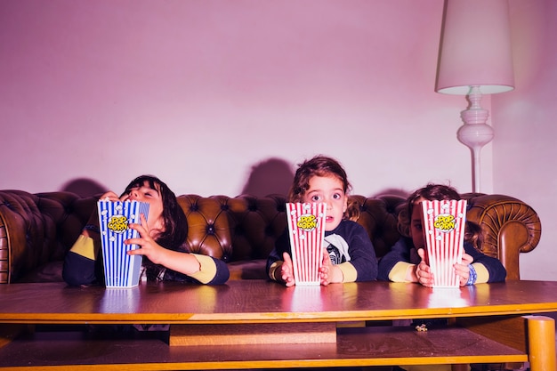 Niños adorables con palomitas de maíz viendo la televisión