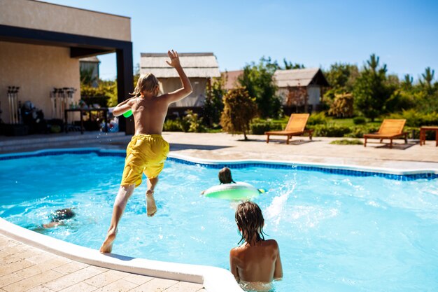 Niños alegres jugando pistolas de agua, regocijándose, saltando, nadando en la piscina.