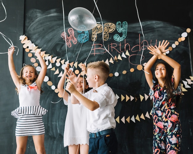 Niños alegres lanzar globos en la fiesta de cumpleaños