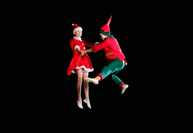 Niños alegres: una niña con un disfraz de Papá Noel y un niño con un disfraz de duende volando juntos