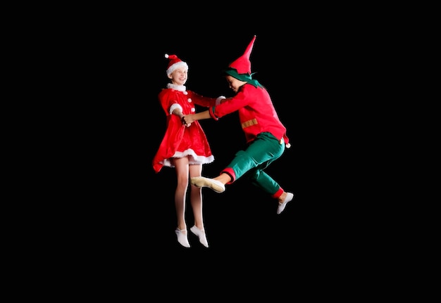 Niños alegres: una niña con un disfraz de Papá Noel y un niño con un disfraz de duende volando juntos