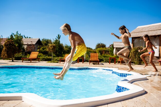 Niños alegres regocijándose, saltando, nadando en la piscina.