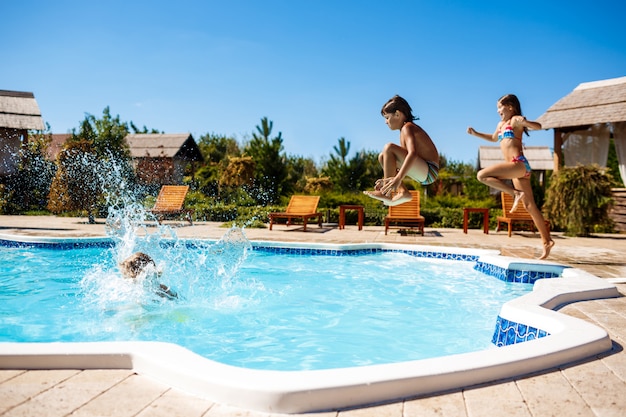 Niños alegres regocijándose, saltando, nadando en la piscina.