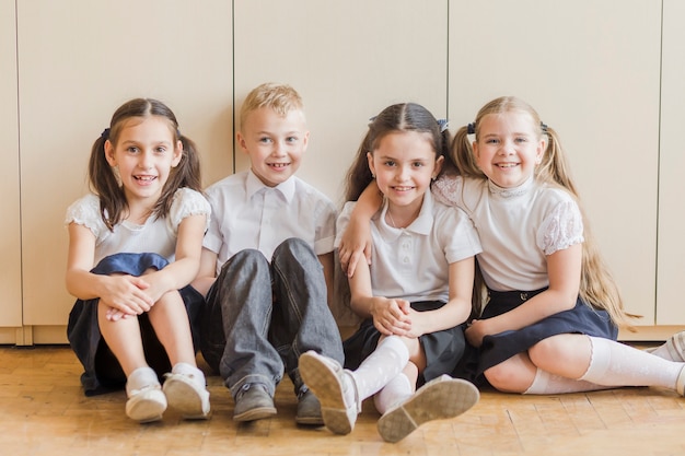 Niños alegres sentados en el piso en la escuela