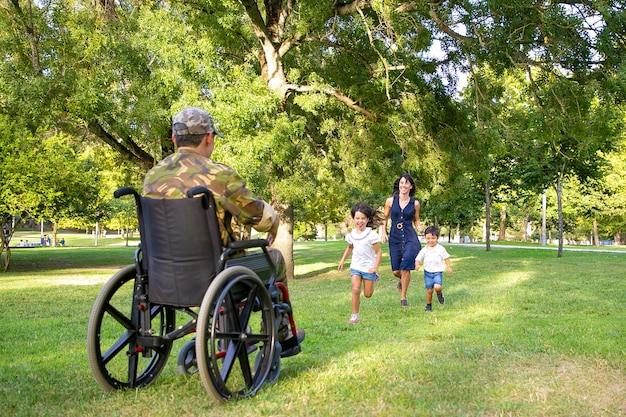 Niños alegres y su mamá se encuentran con un padre militar y corren hacia un hombre discapacitado en camuflaje. Veterano de guerra o concepto de regreso a casa