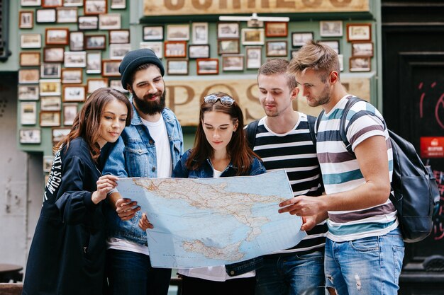 Niños con bolsas y niñas miran el mapa turístico de pie en algún lugar de la ciudad vieja