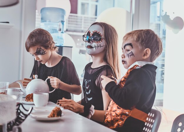 Los niños bonitos con disfraces de Halloween aterradores tienen una fiesta festiva con comida sabrosa y dulces.