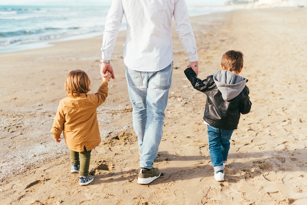 Niños caminando en la playa con papá.