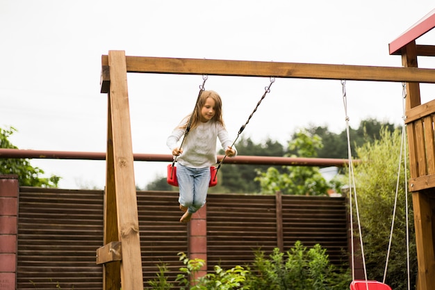 Foto gratuita niños en el columpio. niña columpiándose en un columpio en el patio. verano divertido.