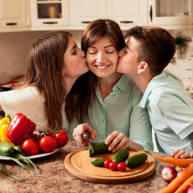 Niños dando un beso a la madre en la cocina mientras preparan la comida