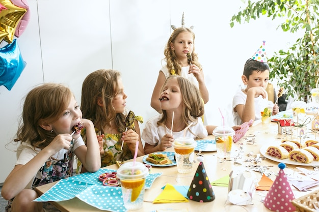 niños y decoraciones de cumpleaños. niños y niñas en la mesa con comida, pasteles, bebidas y artículos de fiesta.