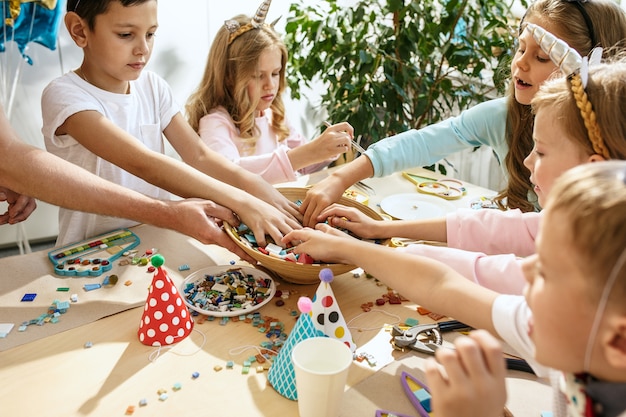 niños y decoraciones de cumpleaños. niños y niñas en la mesa con comida, pasteles, bebidas y artículos de fiesta.