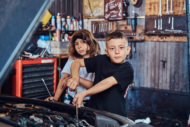 Los niños divertidos y alegres están tratando de arreglar un auto roto en un servicio de autos ocupado.