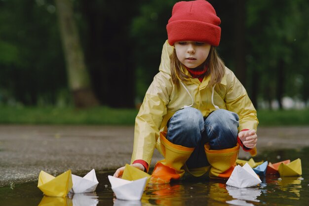 Niños divertidos en botas de lluvia jugando con barco de papel por un charco