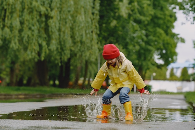 Niños divertidos en botas de lluvia jugando con barco de papel por un charco