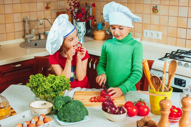 Los niños divertidos de la familia feliz están preparando una ensalada de verduras frescas en la cocina