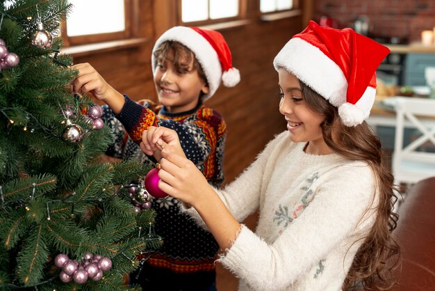 Niños felices de alto ángulo decorando el árbol de navidad