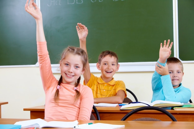 Niños felices con los brazos hacia arriba sentados en el aula