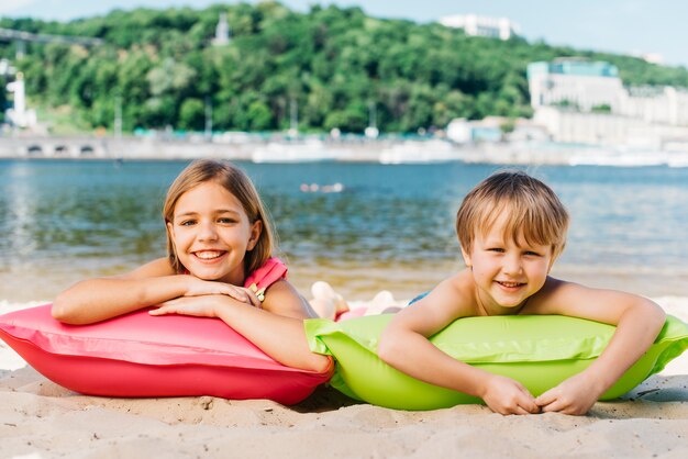 Niños felices descansando en colchones de aire en la costa del río en verano