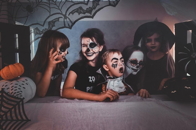 Niños felices con espeluznantes disfraces de Halloween y maquillaje disfrutando de su pequeña fiesta.