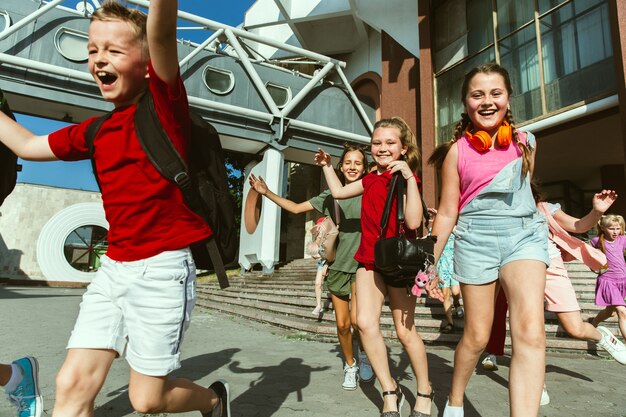 Niños felices jugando en la calle de la ciudad en un día soleado de verano frente a un edificio moderno. Grupo de niños felices o adolescentes divirtiéndose juntos. Concepto de amistad, infancia, verano, vacaciones.