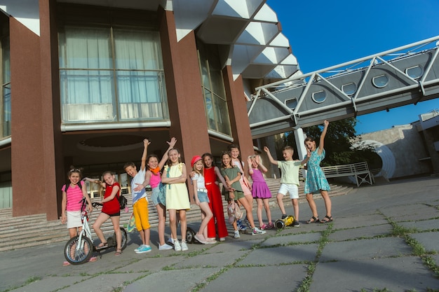 Niños felices jugando en la calle de la ciudad en un día soleado de verano frente a un edificio moderno. Grupo de niños felices o adolescentes divirtiéndose juntos. Concepto de amistad, infancia, verano, vacaciones.