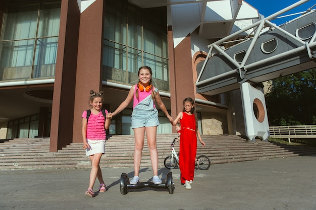 Niños felices jugando en la calle de la ciudad en un día soleado de verano frente a un edificio moderno. Grupo de niños felices o adolescentes divirtiéndose juntos