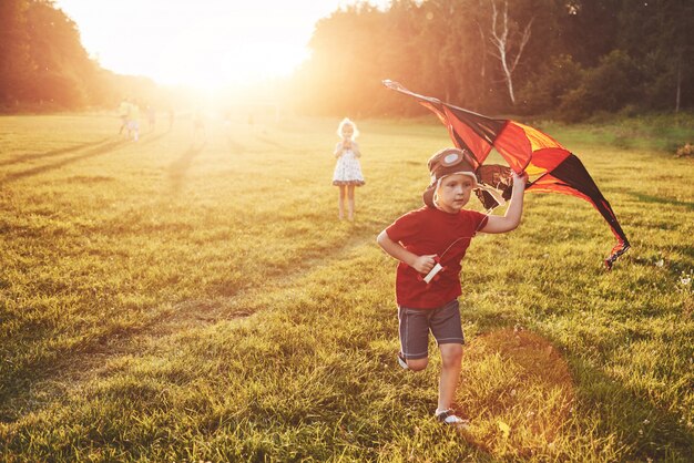 Niños felices lanzan una cometa en el campo al atardecer. Pequeño niño y niña en vacaciones de verano