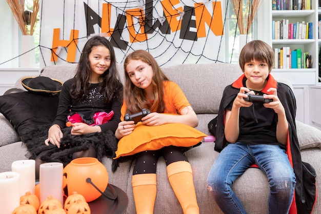 Los niños felices, niños y niñas disfrazados de Halloween, disfrutan jugando con joystick en la mano