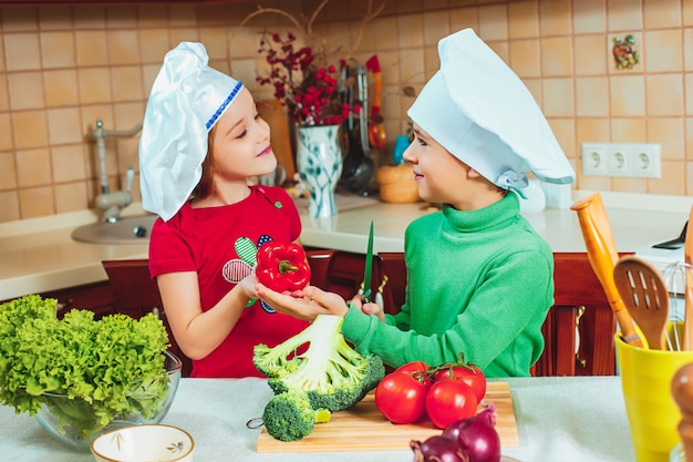 Foto gratuita niños felices preparan ensalada de vegetales frescos en la cocina