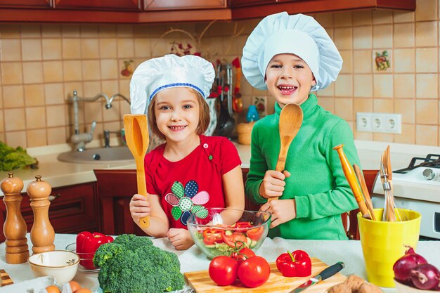 Niños felices preparan ensalada de vegetales frescos en la cocina